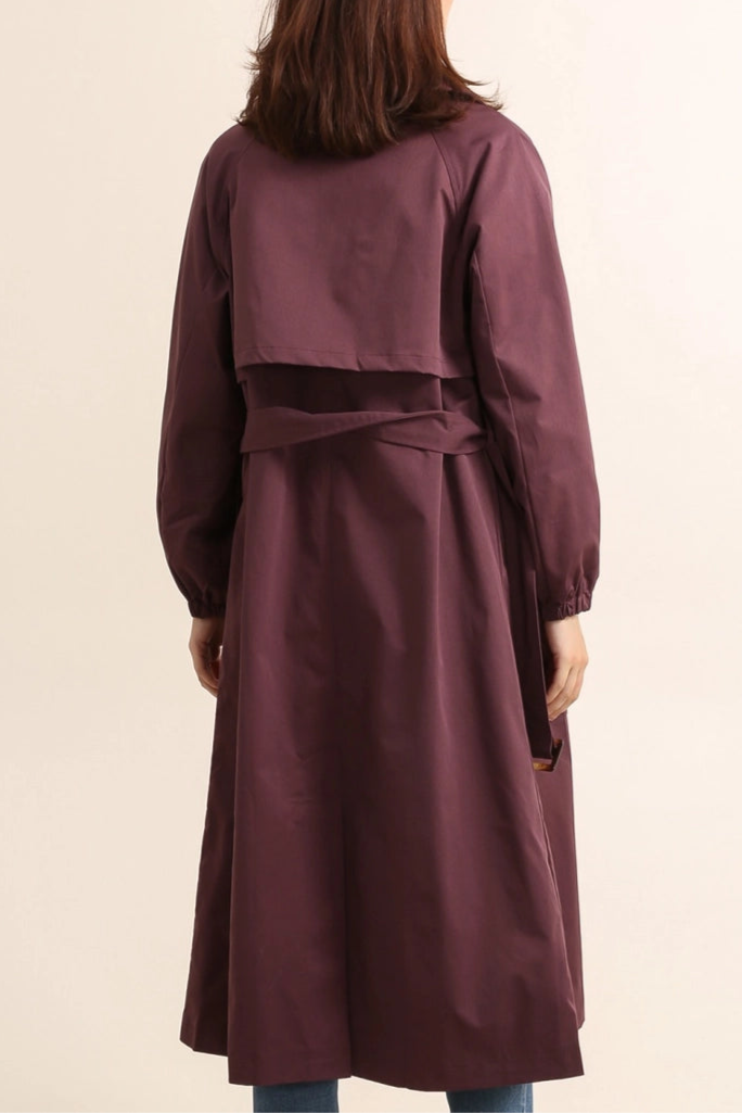 Woman wearing a becky burgundy trench coat over a black sweater and dark jeans on a plain background by penn and reid boutique leighton buzzard