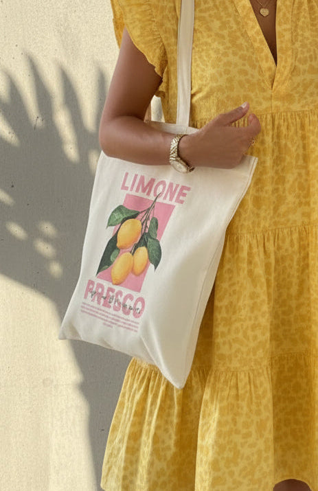 Person holding a tote bag with 'Limone' design and a woman in a yellow dress taking a selfie.
