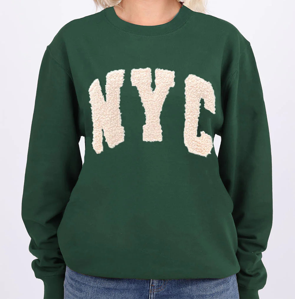 Person wearing a green sweatshirt with 'NYC' on it against a white background