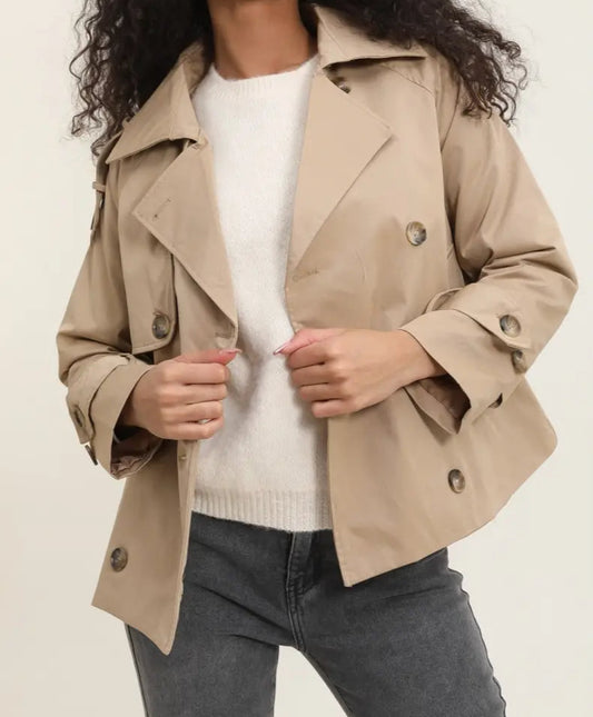 Woman wearing a sarah beige trench coat over a white sweater and dark jeans on a plain background by penn and reid boutique leighton buzzard

